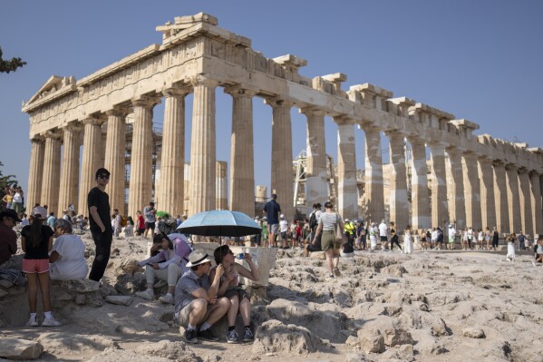 A tourist drinks water as she and a man sit under an umbrella in front of the five century BC Parthenon temple at the Acropolis hill during a heat wave, on July 13, 2023. (AP Photo/Petros Giannakouris, File)