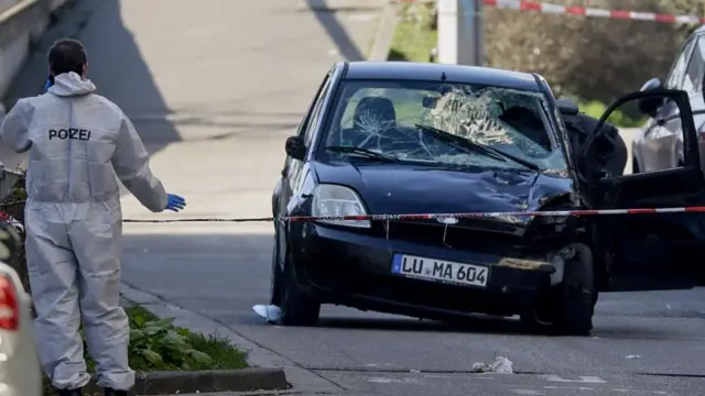 A damaged, black car at the scene of the attack, cordoned off by police tape.