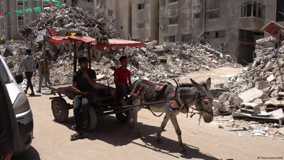 Dy njerëz me karrocë duke kaluar para ndërtesave të shkatërruara në Rripin e Gazës