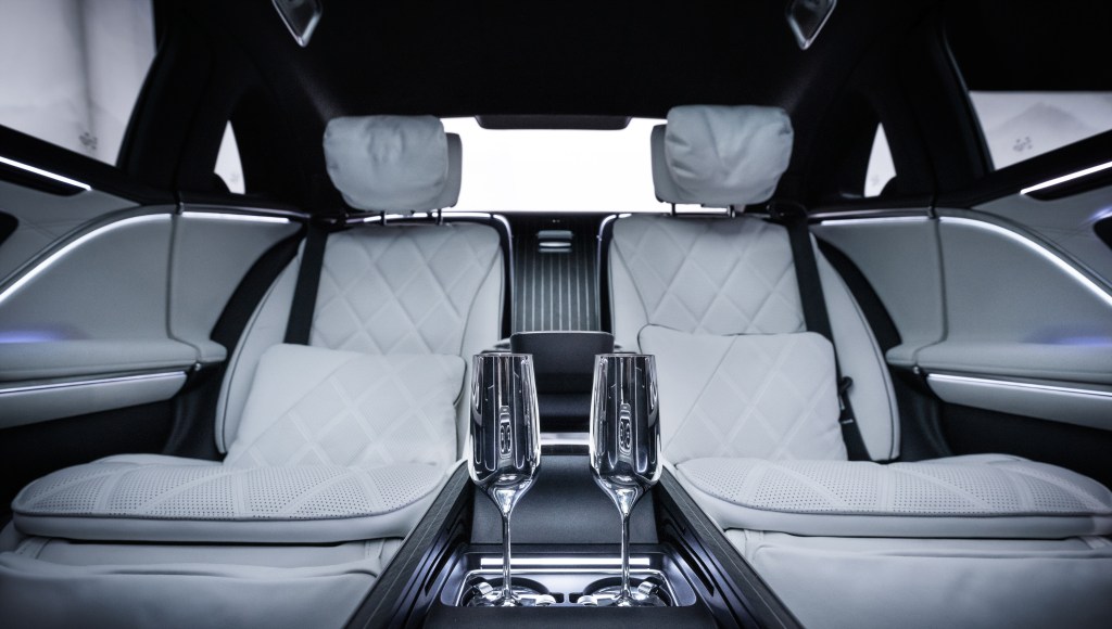 The interior of a Maybach S-Class, with champagne flutes on a console between two luxurious white seats.