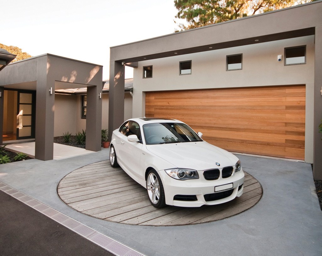 White BMW on a wooden car turntable in front of a modern house.